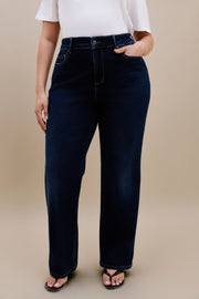 Bottom half of a woman wearing white t-shirt and dark straight leg jeans with a beige background
