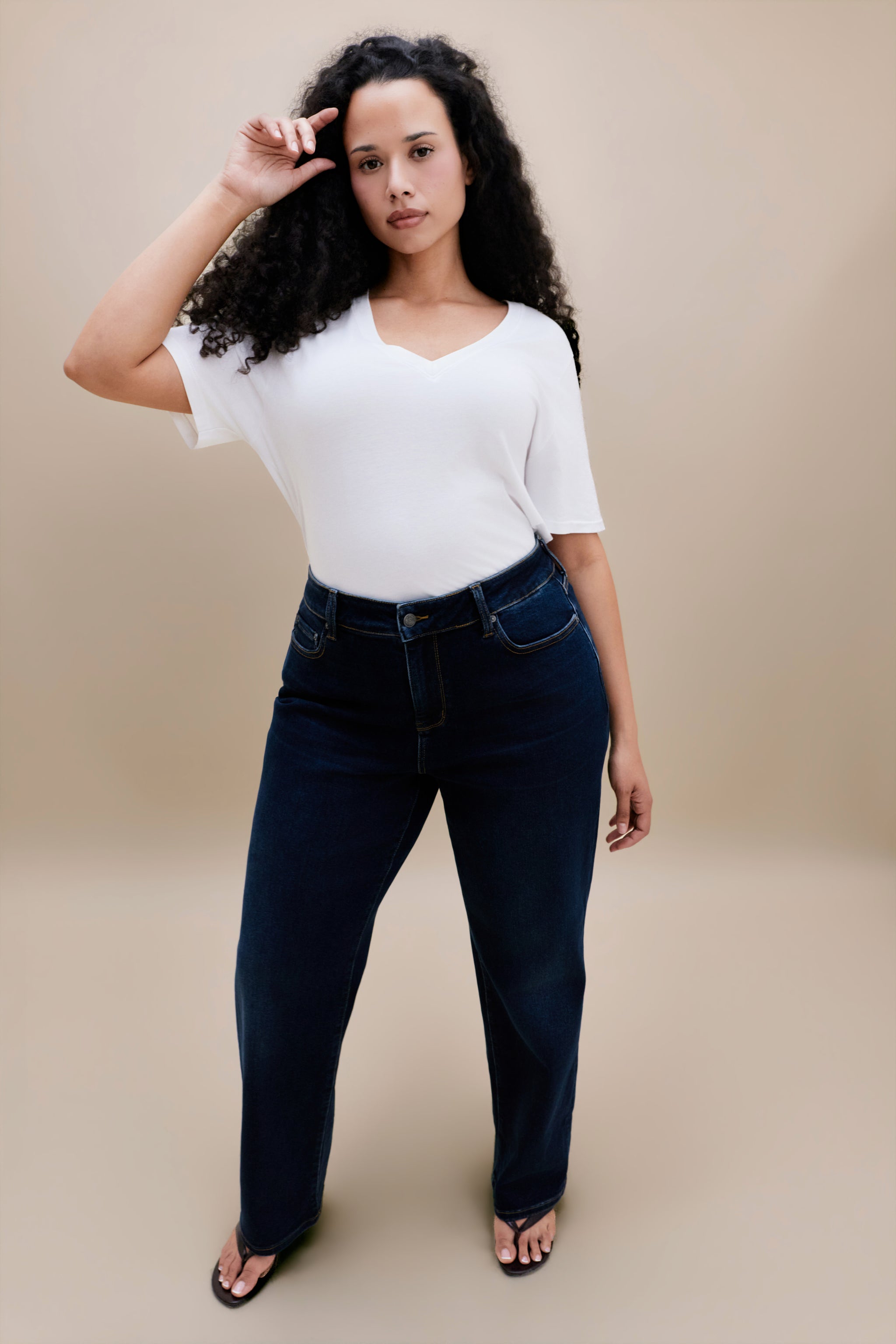 Woman wearing a plain white t-shirt and dark jeans against a beige background