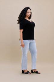 Woman wearing a black t-shirt and light blue jeans against a beige background