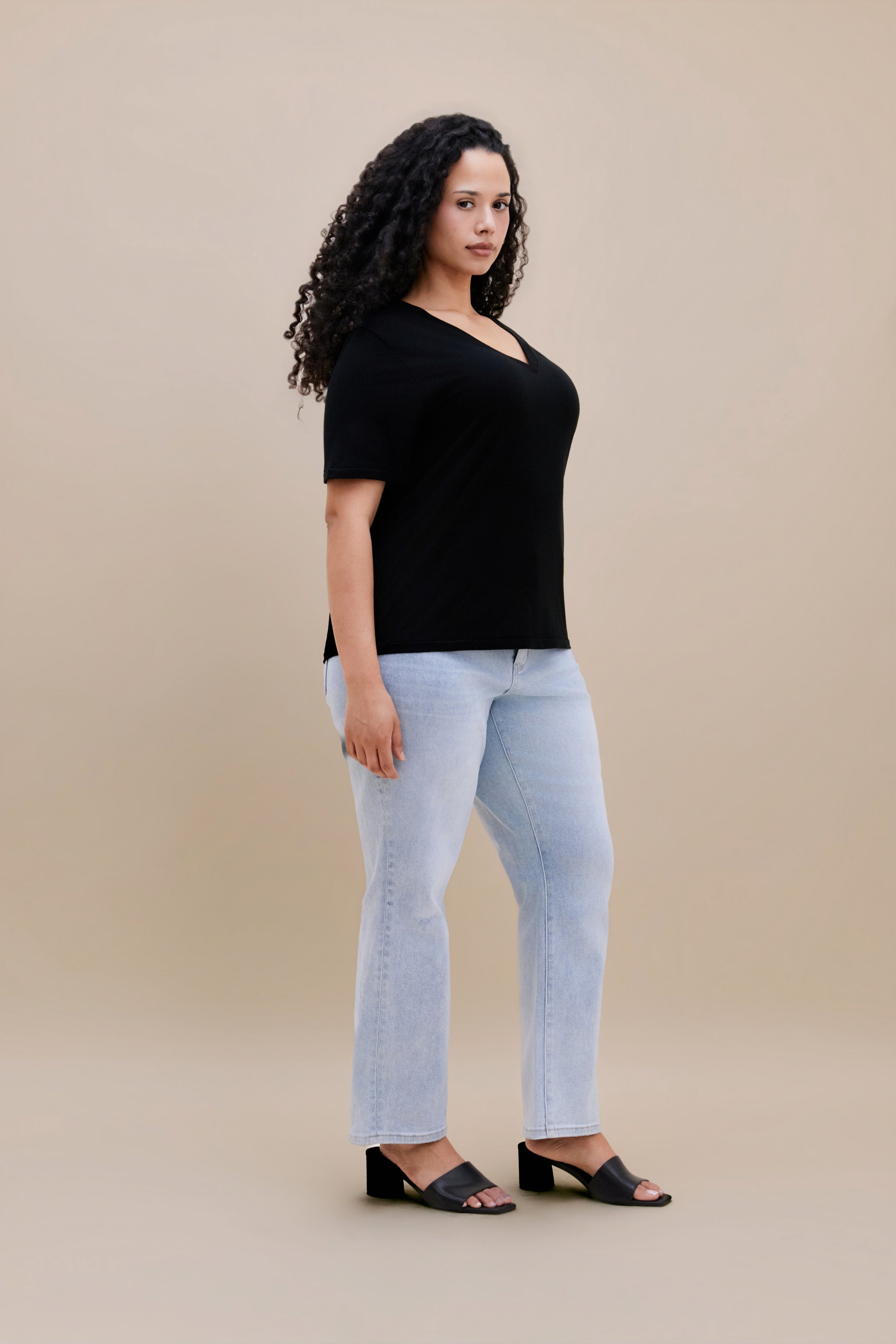 Woman wearing a black t-shirt and light blue jeans against a beige background