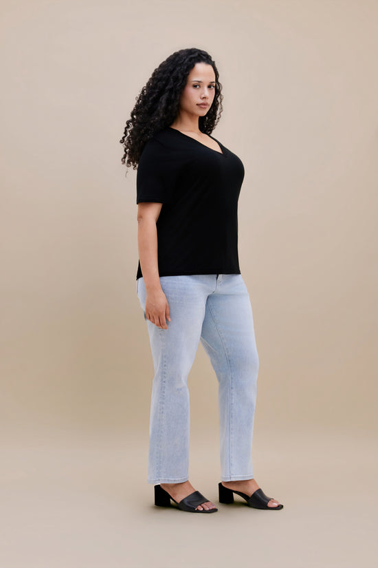 Woman wearing a black t-shirt and light blue jeans against a beige background