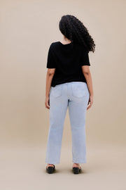 Woman wearing a black t-shirt and light blue jeans against a beige background