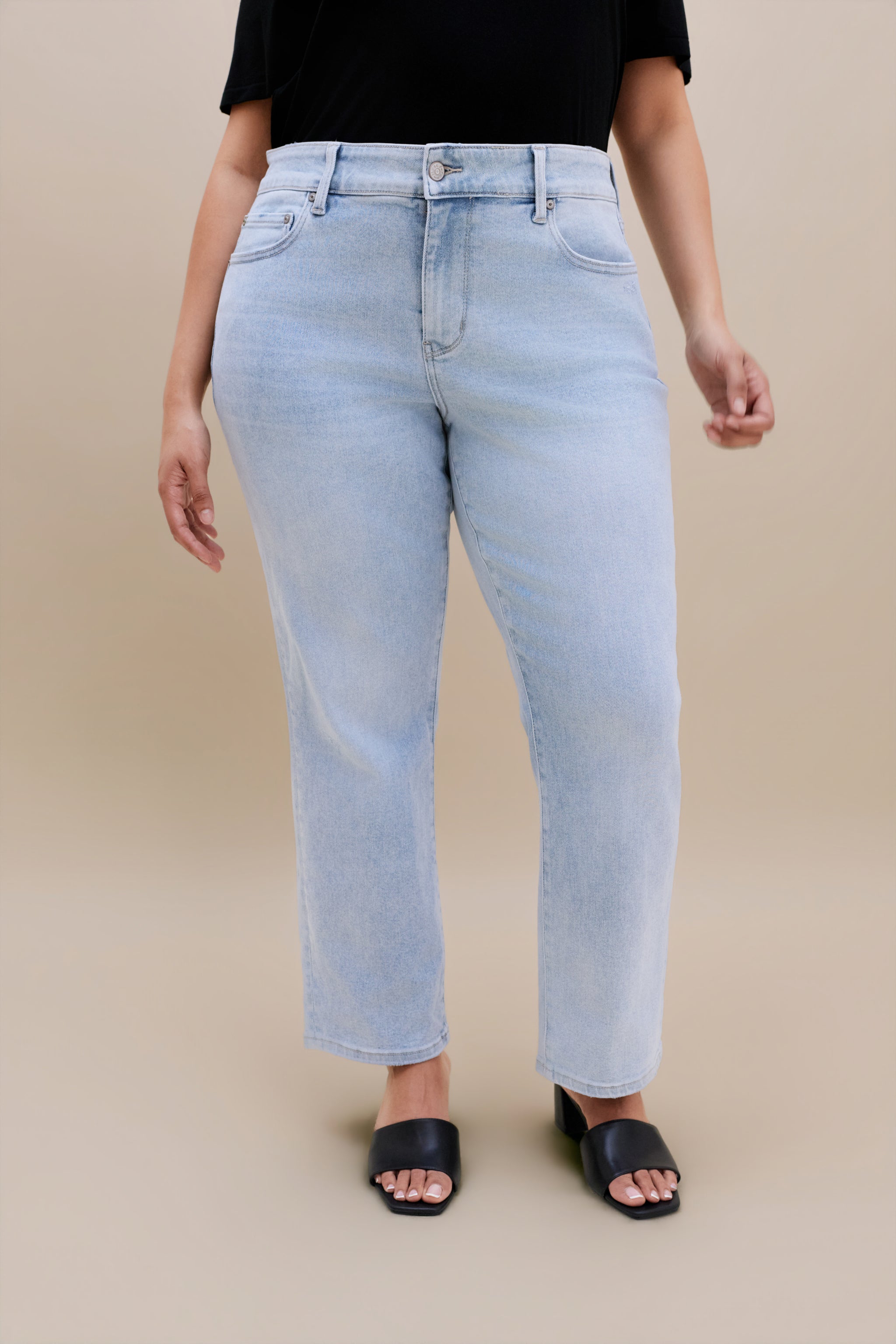 Woman wearing a black t-shirt and light blue jeans against a beige background