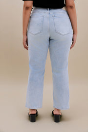 Woman wearing a black top light colored jeans with a beige background 