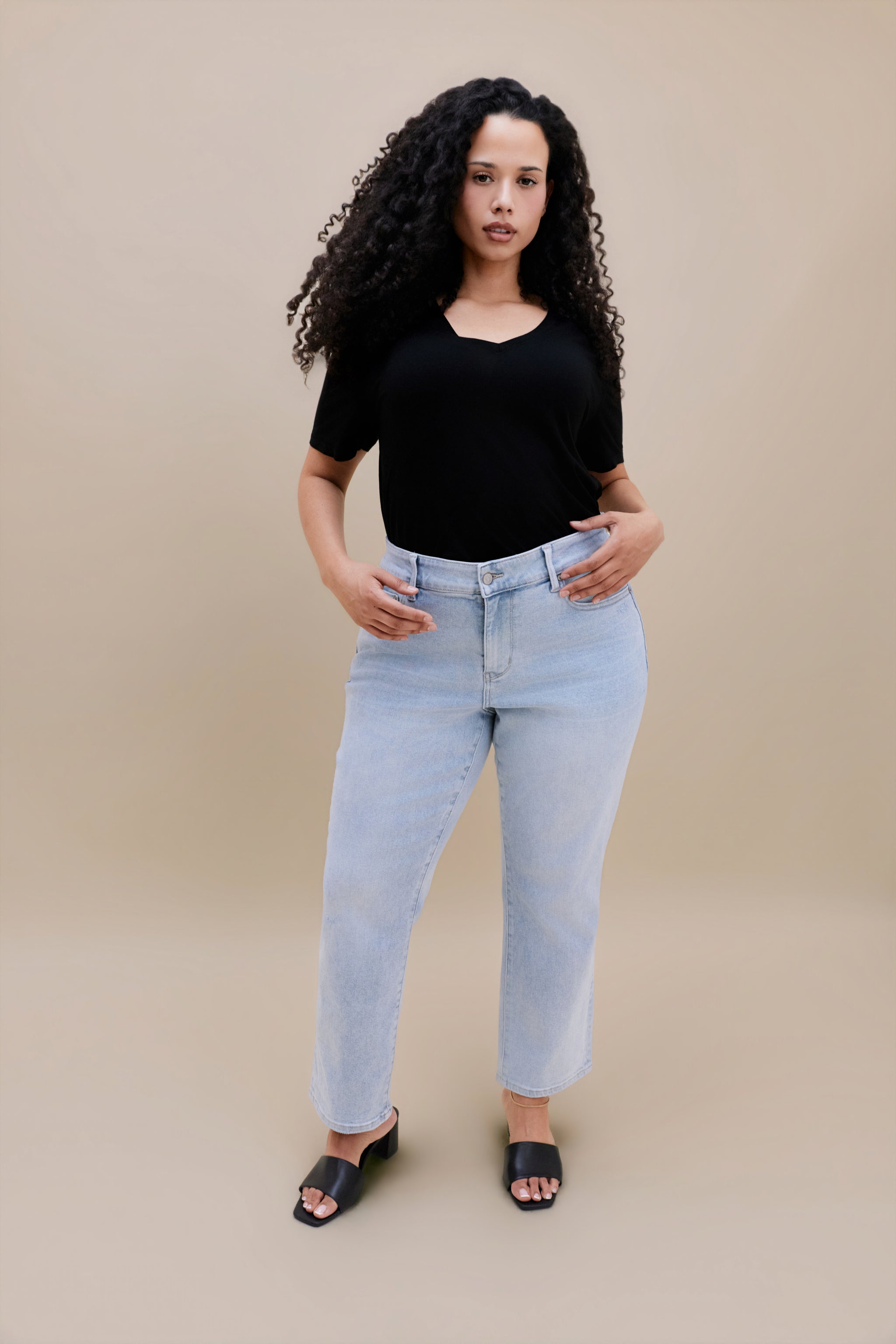 Woman wearing a black t-shirt and light blue jeans against a beige background | model-size: 16