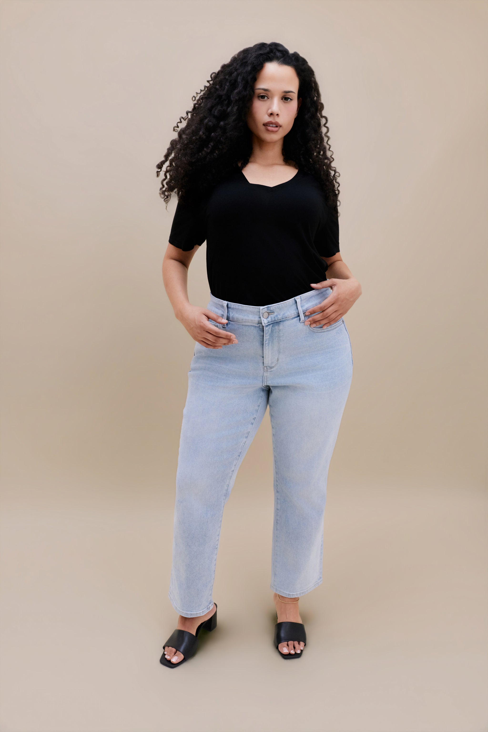 Woman wearing a black t-shirt and light blue jeans against a beige background