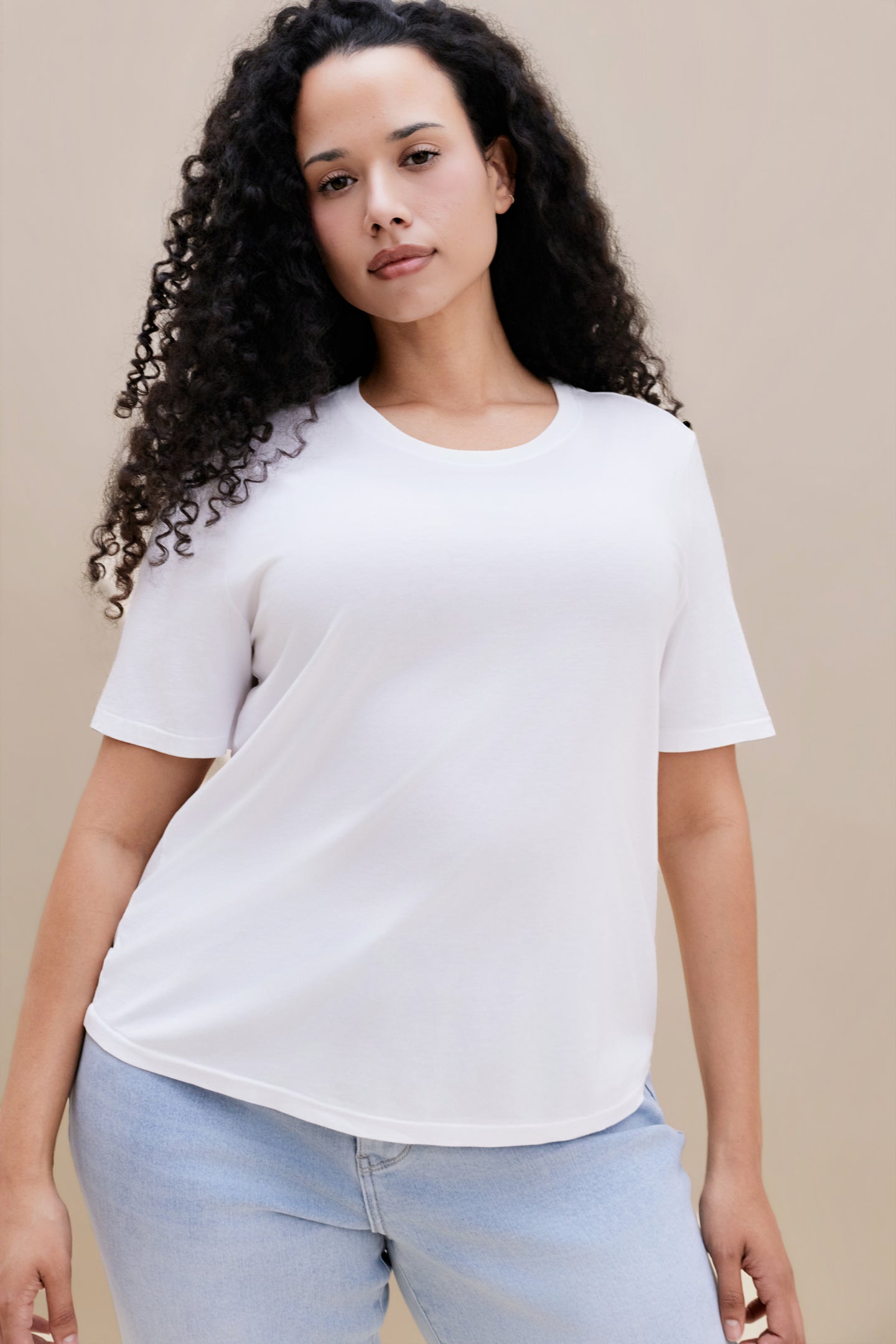 Woman wearing a white t-shirt and light blue jeans against a beige background | model-size: 16