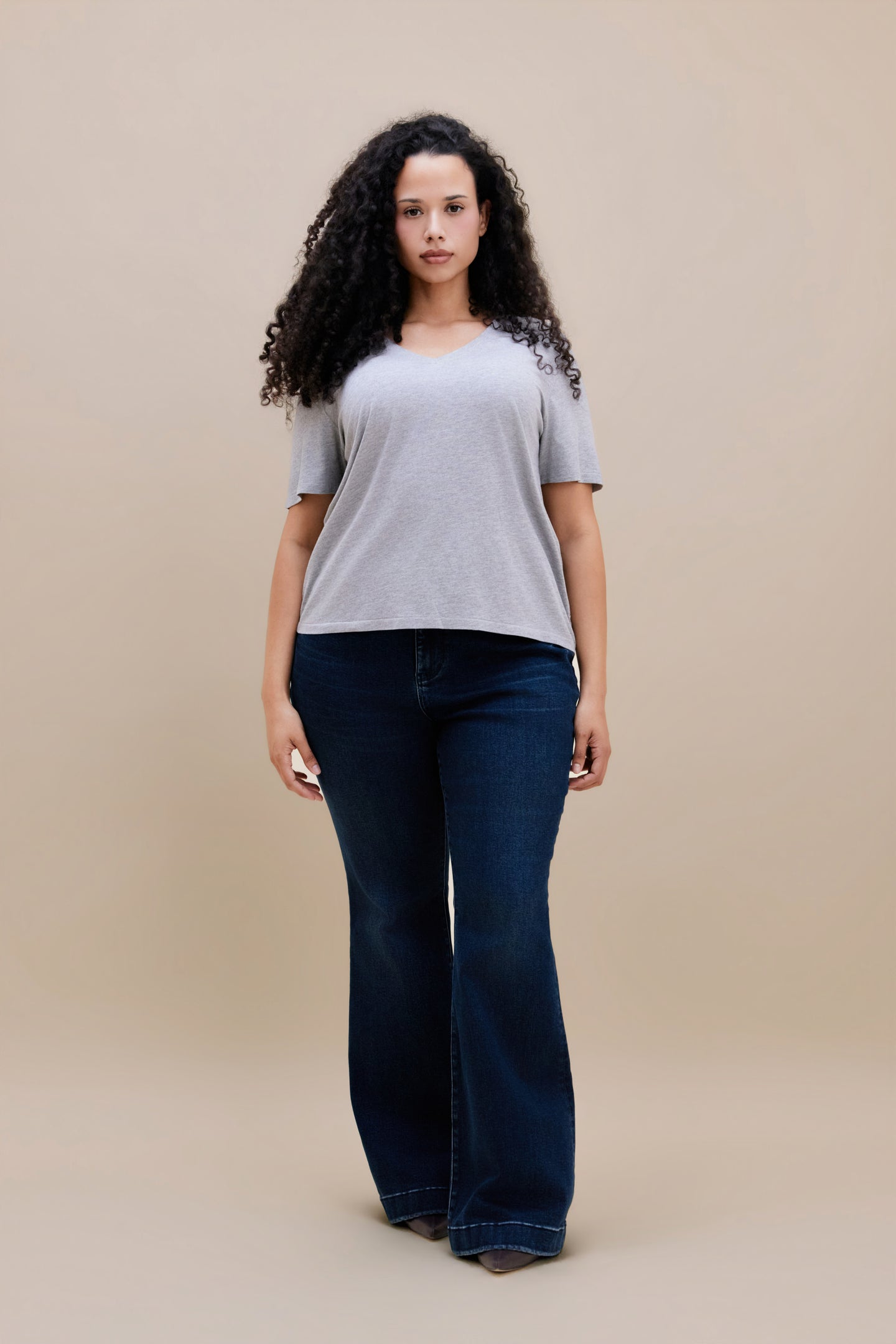 Woman wearing a heather grey v-neck t-shirt and dark jeans