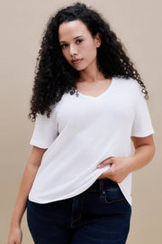 Woman wearing a plain white t-shirt and dark jeans against a beige background | model-size: 16