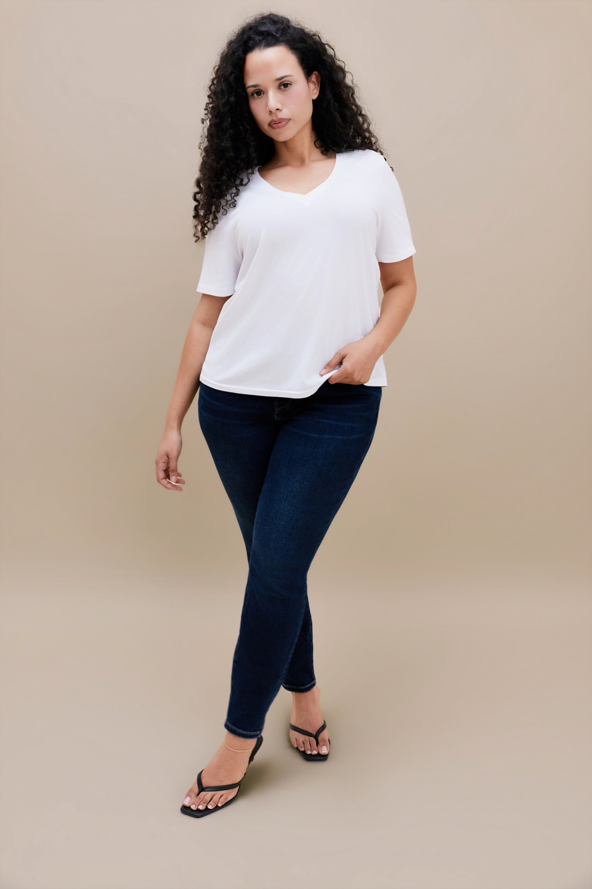 Woman wearing a plain white t-shirt and dark jeans against a beige background
