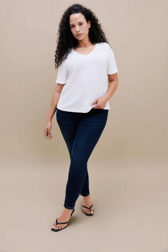 Woman wearing a plain white t-shirt and dark jeans against a beige background