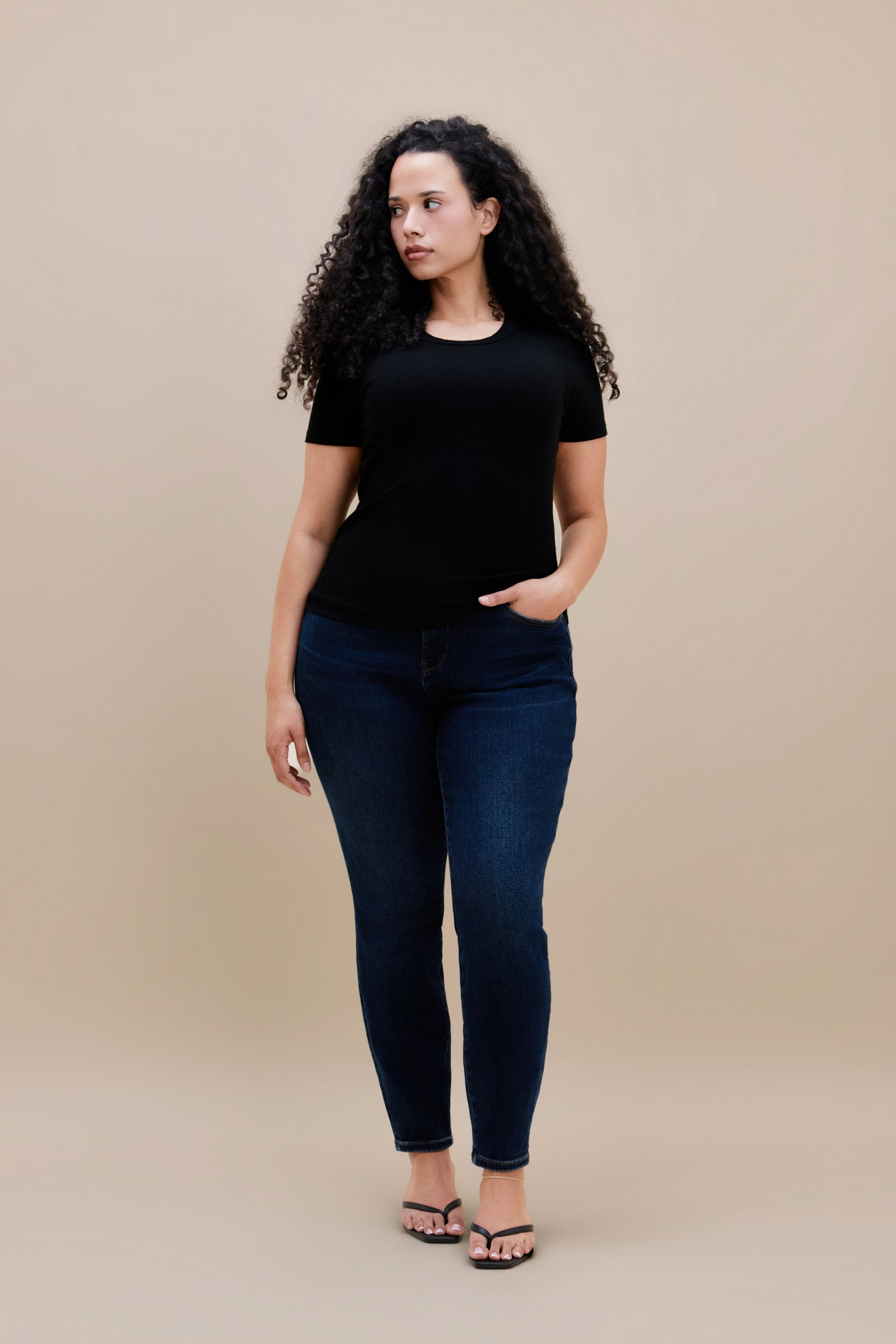 Woman wearing a black t-shirt and dark skinny jeans with a beige background | model-size: 16
