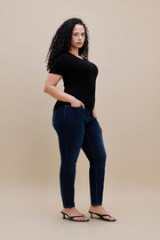 Woman wearing a black t-shirt and dark skinny jeans with a beige background 
