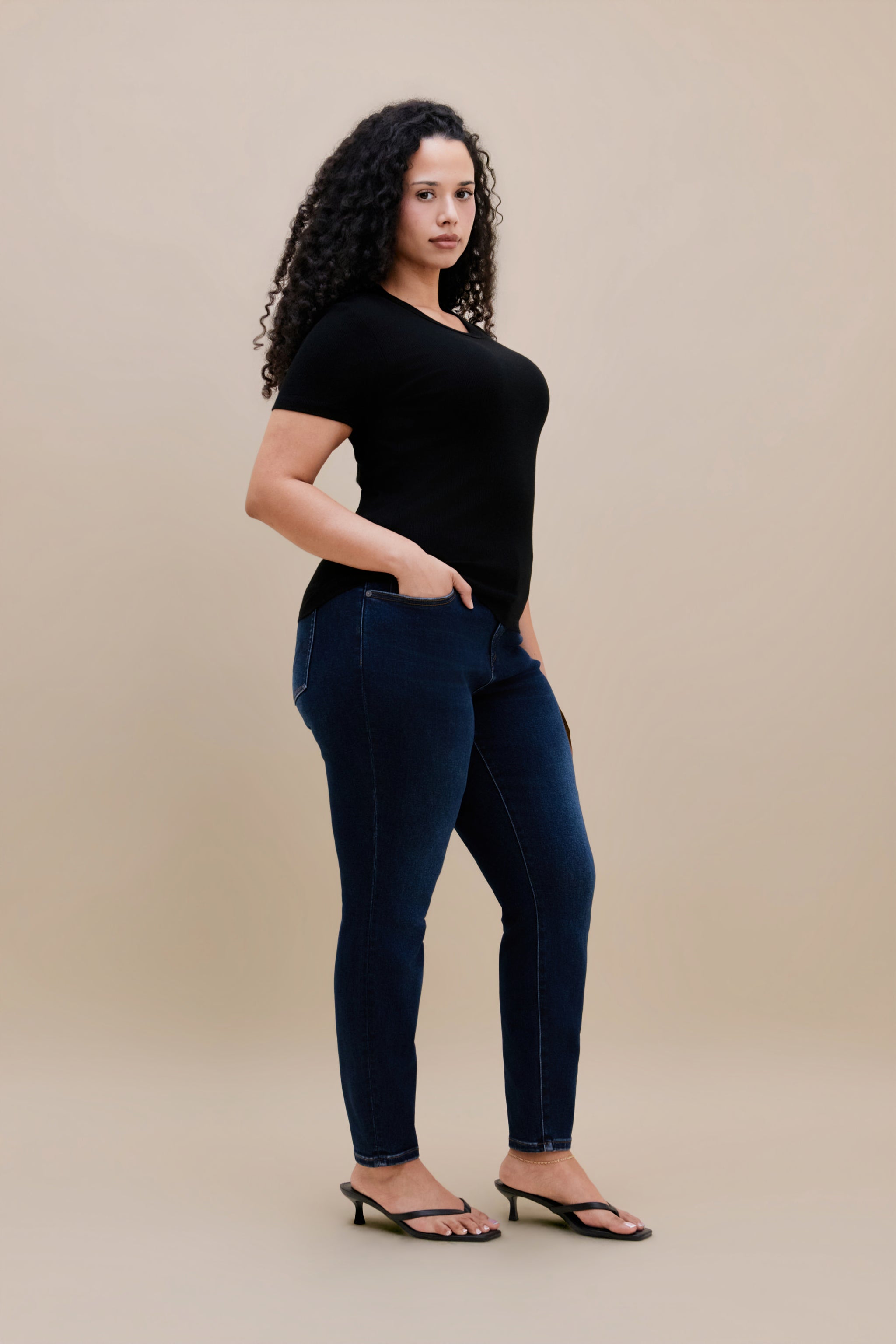 Woman wearing a black t-shirt and dark skinny jeans with a beige background 
