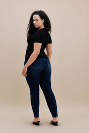 Backside of a woman wearing a black t-shirt and dark skinny jeans with a beige background 