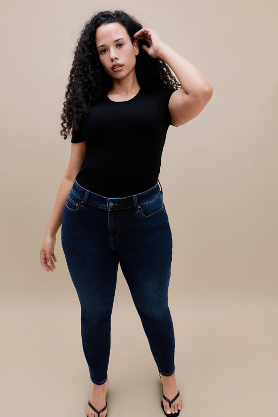 Woman wearing a black t-shirt and dark skinny jeans with a beige background 