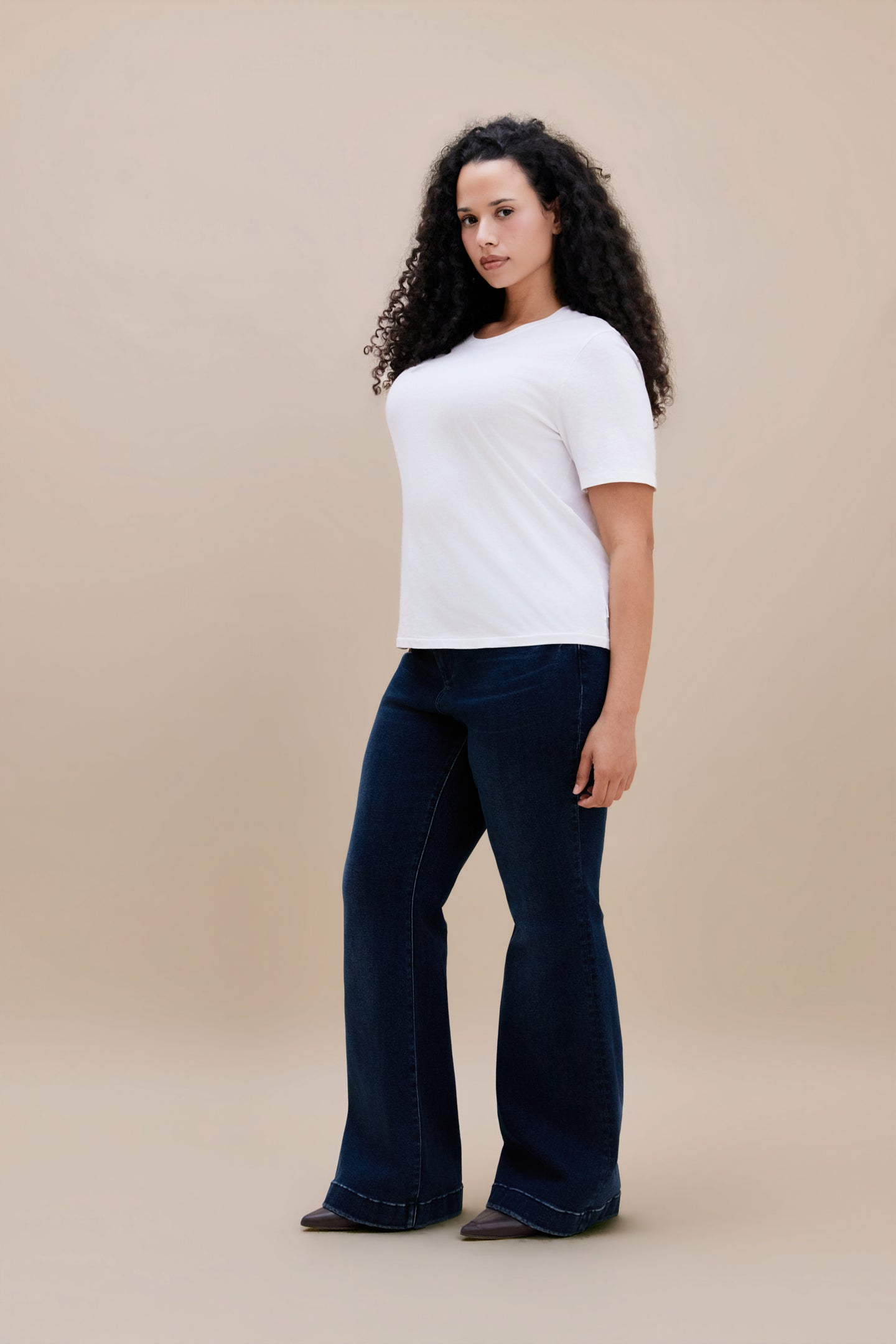 Woman wearing a white t-shirt and dark flare jeans with a beige background