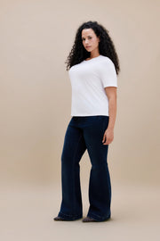 Woman wearing a white t-shirt and dark flare jeans with a beige background