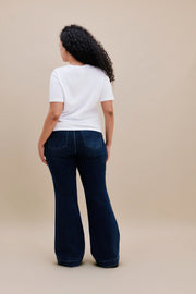 Woman wearing a white t-shirt and dark flare jeans with a beige background