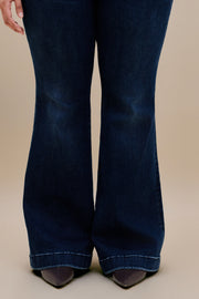 Woman wearing dark flare jeans with a beige background