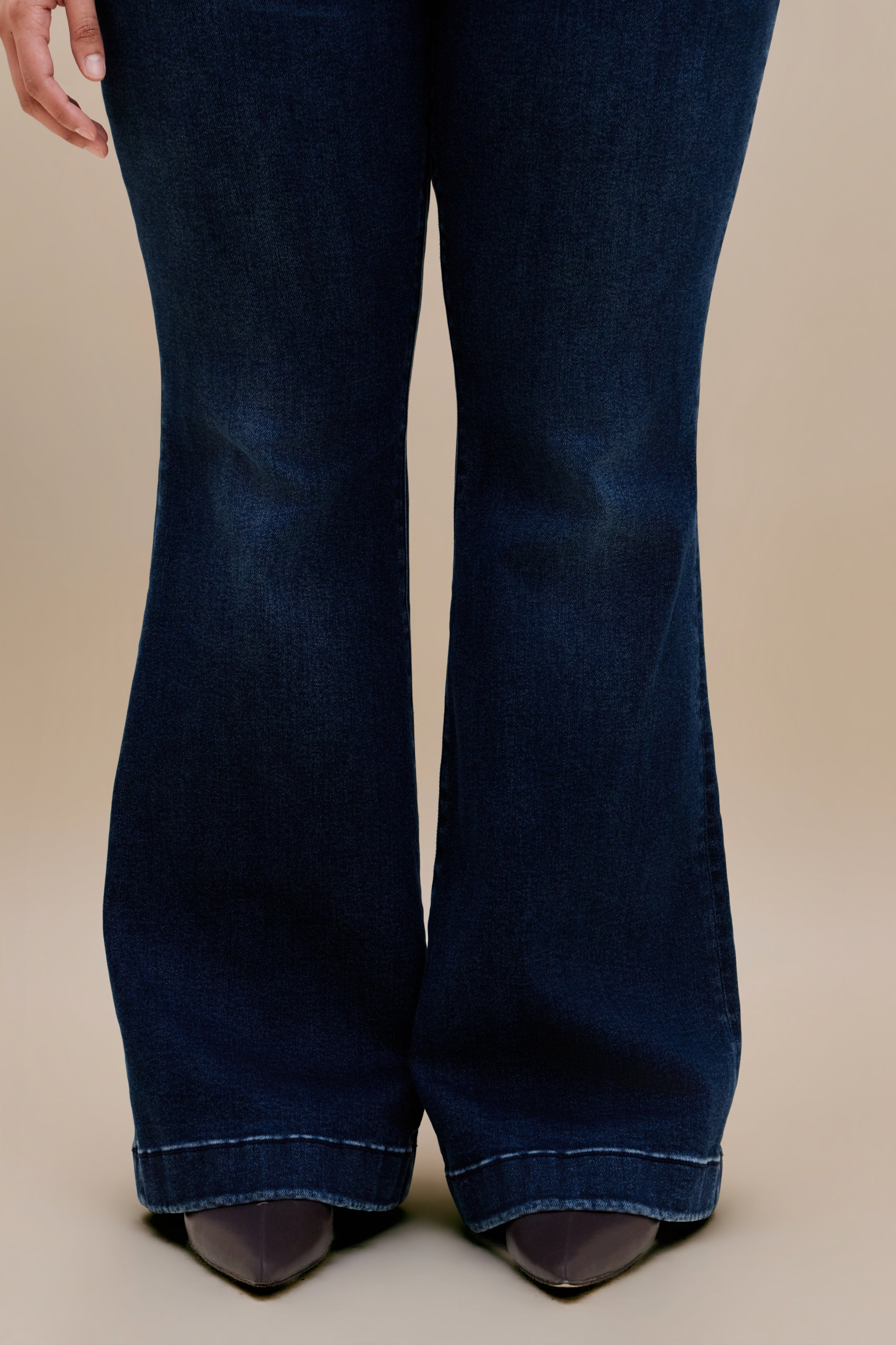 Woman wearing dark flare jeans with a beige background