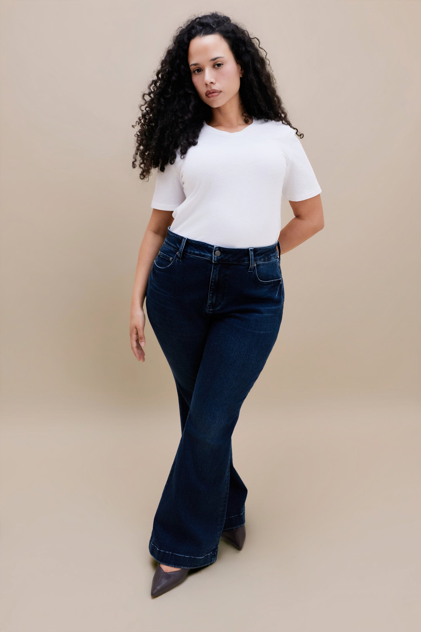 Woman wearing a white t-shirt and dark flare jeans with a beige background