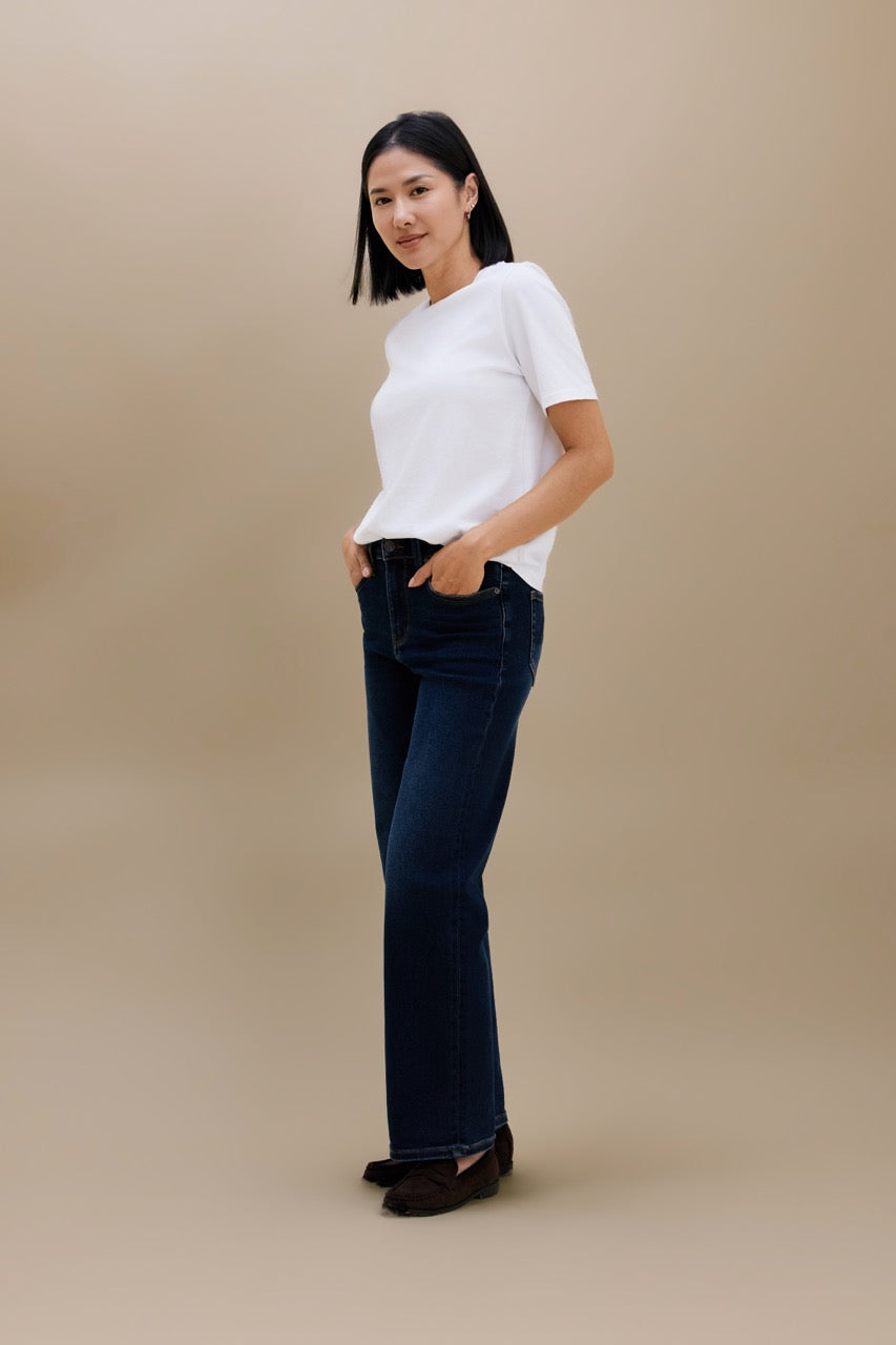 A woman modeling a white short-sleeve crewneck t-shirt and dark blue straight leg jeans against a solid beige studio background.
