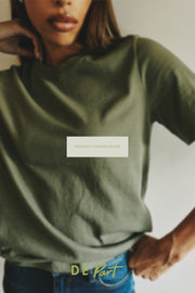 A cropped lifestyle photo of a model wearing an olive green t-shirt and blue jeans, with a 'IMAGERY COMING SOON' placeholder overlay in the center and a 'DE'PART' brand logo at the bottom.