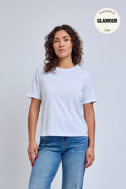 Woman wearing a plain white t-shirt and blue jeans against a light gray background. 