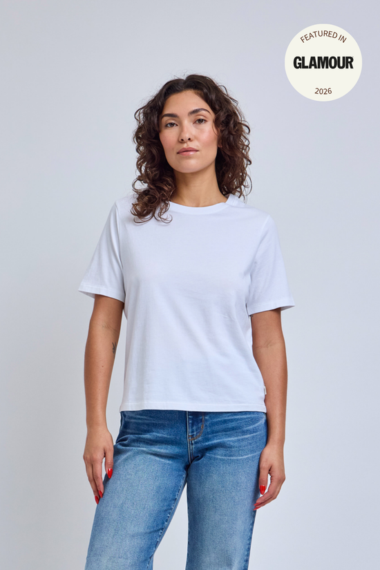 Woman wearing a plain white t-shirt and blue jeans against a light gray background. 