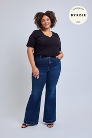 Woman wearing a black top and blue jeans on a light gray background.