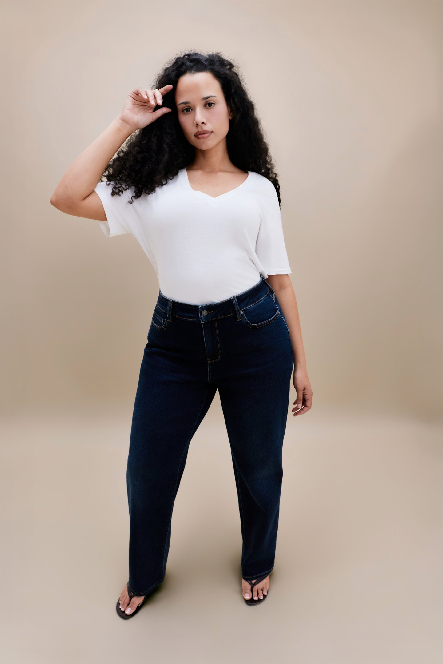 Woman wearing white t-shirt and dark straight leg jeans with a beige background | model-size: 16