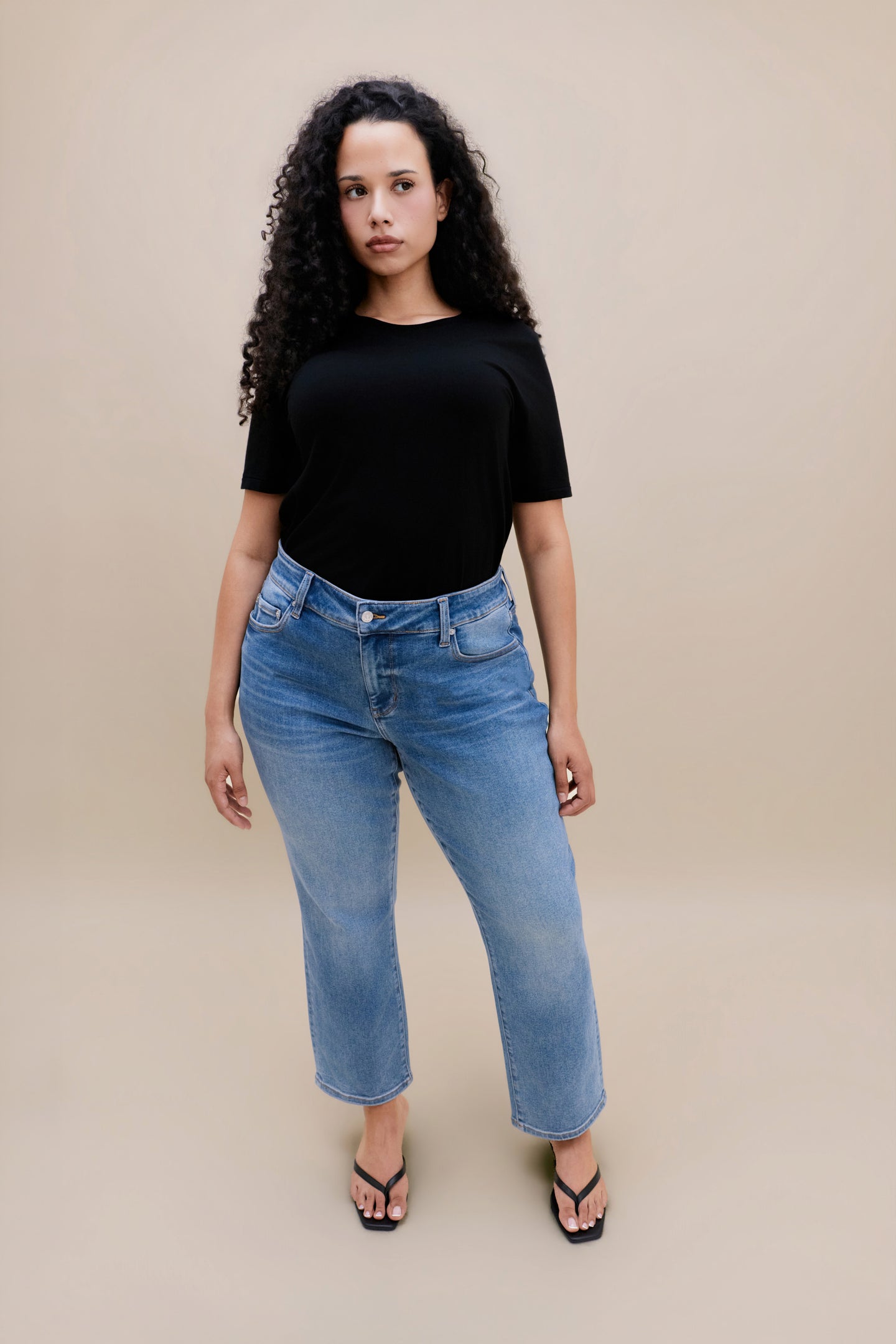 Woman wearing a black t-shirt and jeans with a beige background