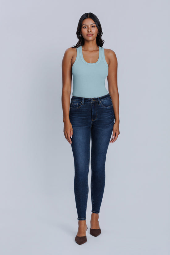 Woman wearing a light blue tank top and dark blue skinny jeans against a light gray background | model-size: 4