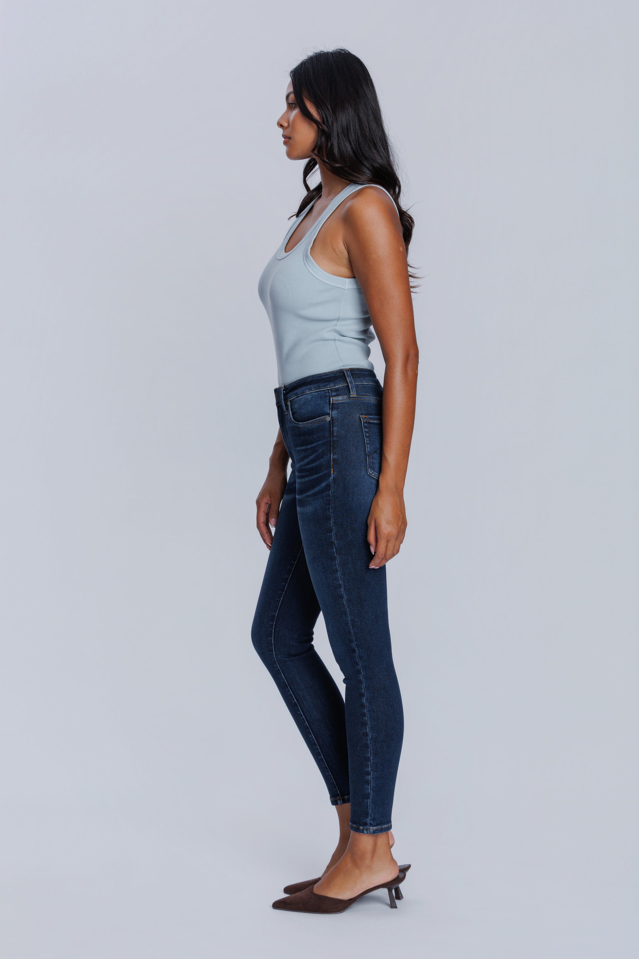 Woman wearing a DePart light blue tank top and dark blue skinny jeans against a light gray background