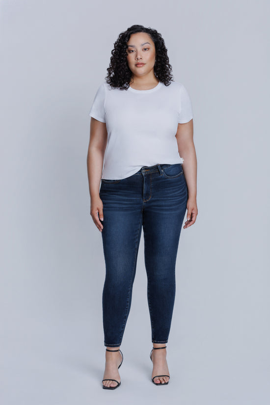 Woman wearing a DePart white tee and dark blue skinny jeans against a light gray background | model-size: 16