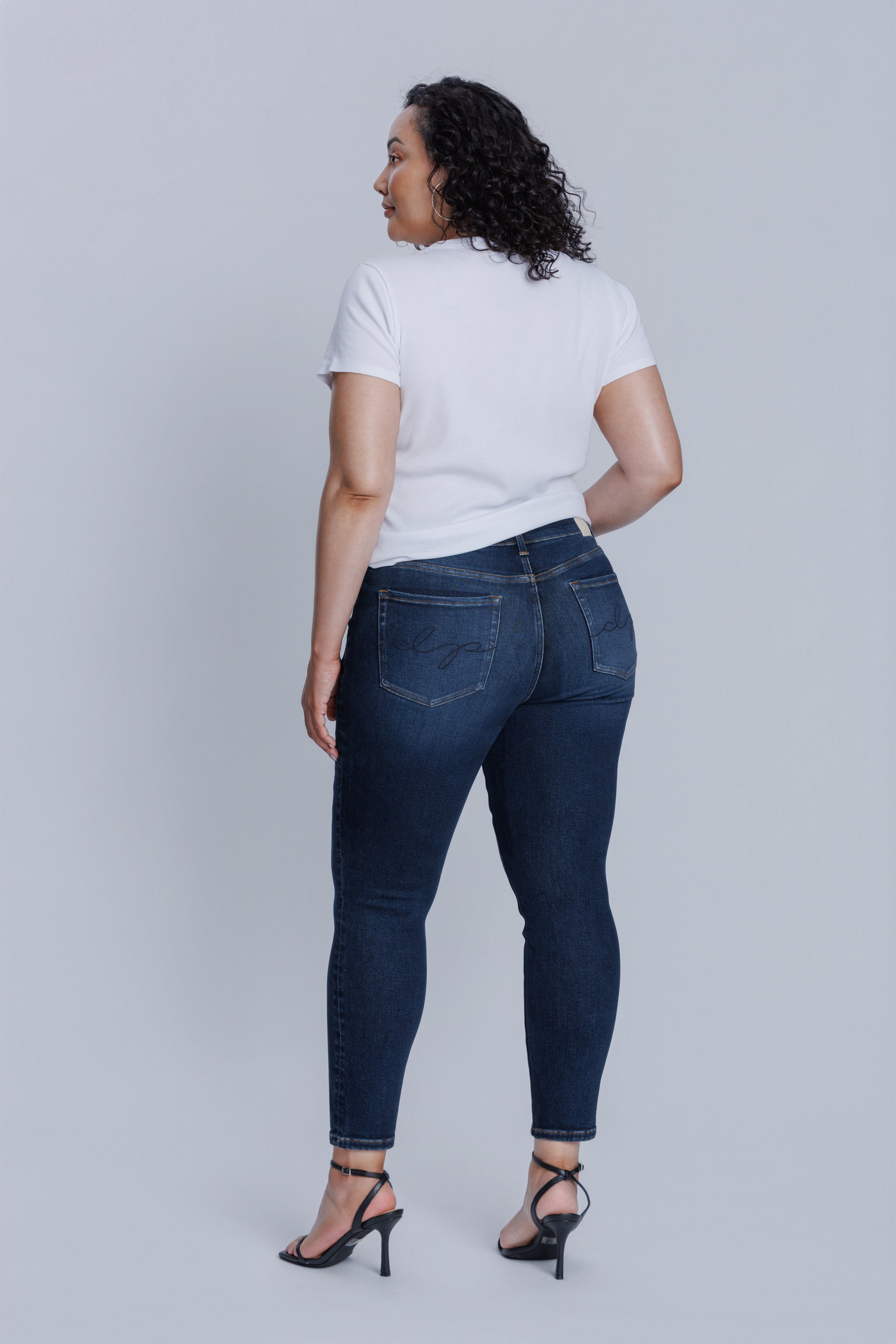 Woman wearing a DePart white tee and dark blue skinny jeans against a light gray background
