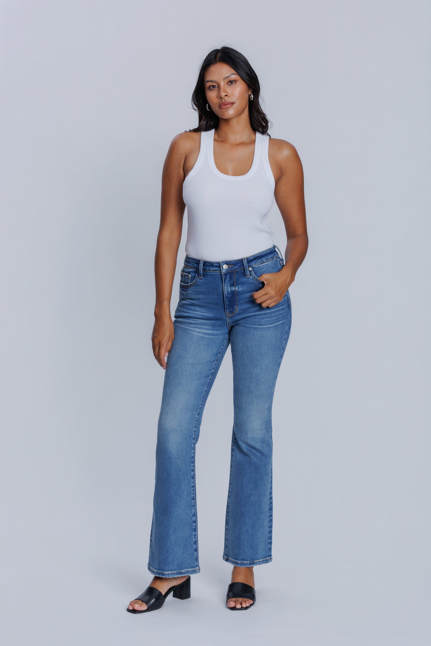 Woman wearing a DePart white tank top and blue flare jeans against a light gray background | model-size: 4