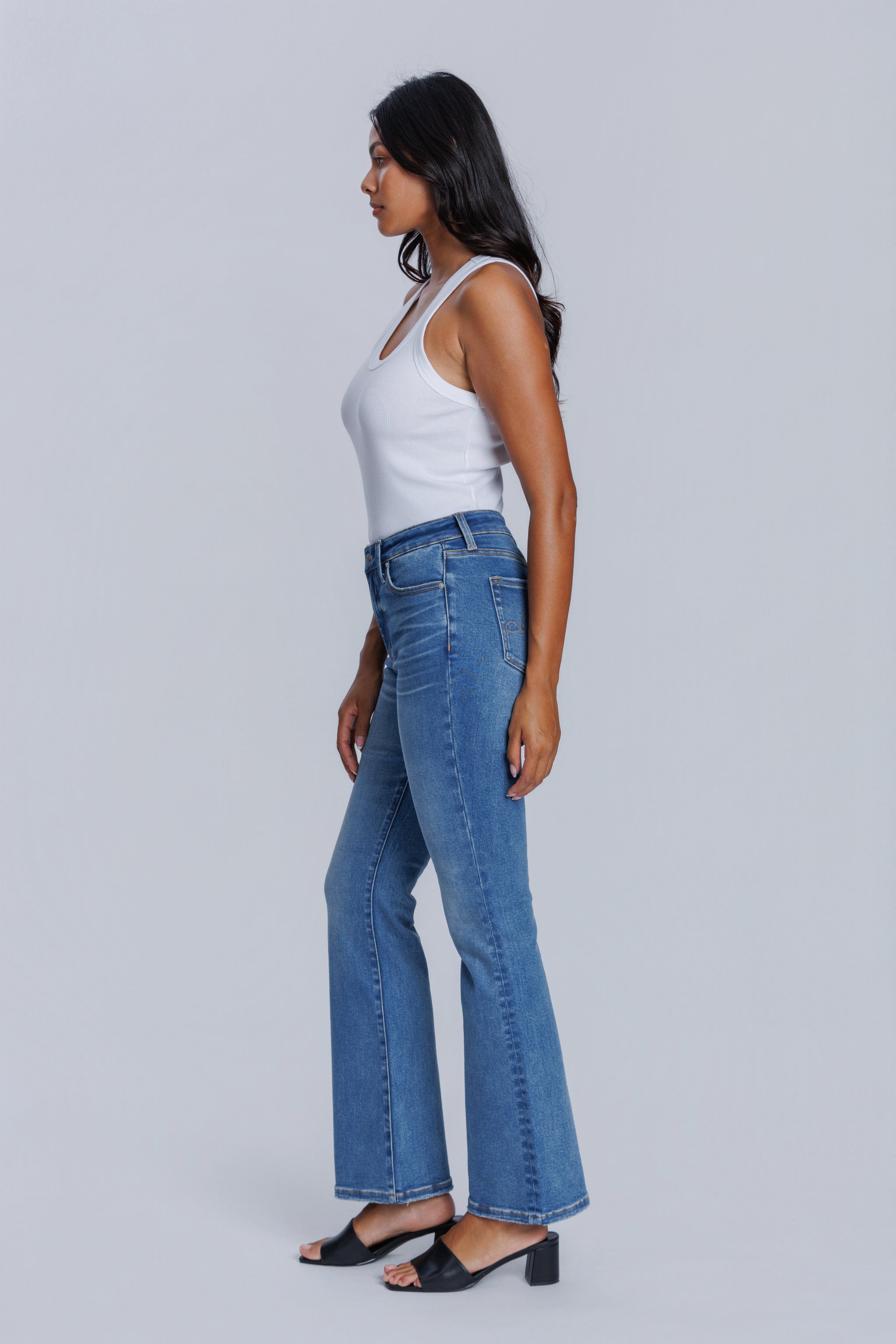 Woman wearing a DePart white tank top and blue flare jeans against a light gray background