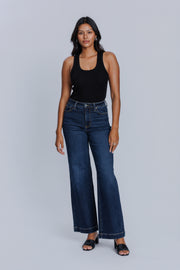 Woman wearing a DePart white tank top and dark blue wide leg jeans against a light gray background | model-size: 4