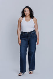 Woman wearing a DePart white tank top and dark blue jeans against a light gray background | model-size: 16
