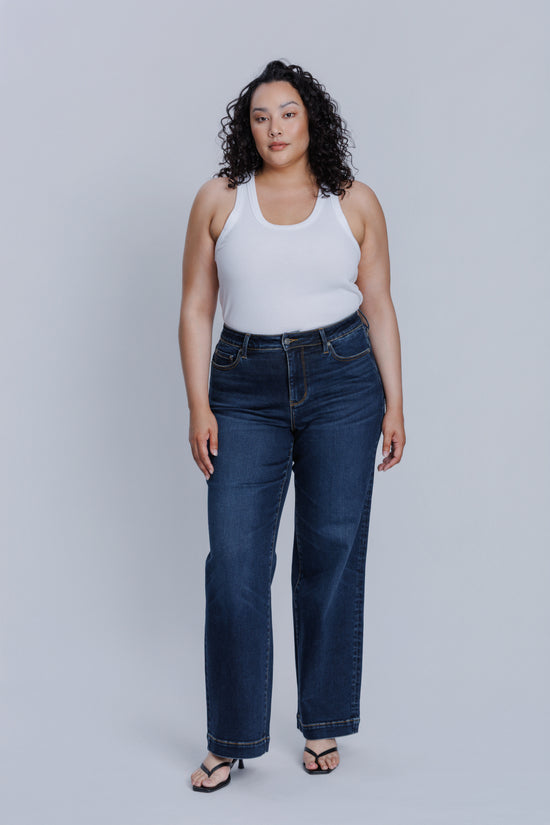 Woman wearing a DePart white tank top and dark blue jeans against a light gray background | model-size: 16