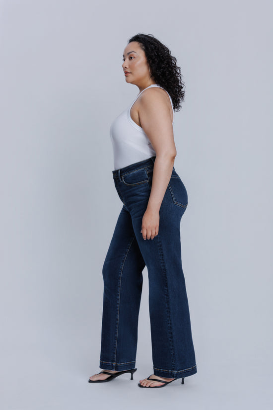 Woman wearing a DePart white tank top and dark blue jeans against a light gray background