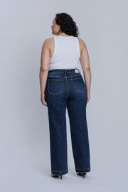 Woman wearing a DePart white tank top and dark blue jeans against a light gray background