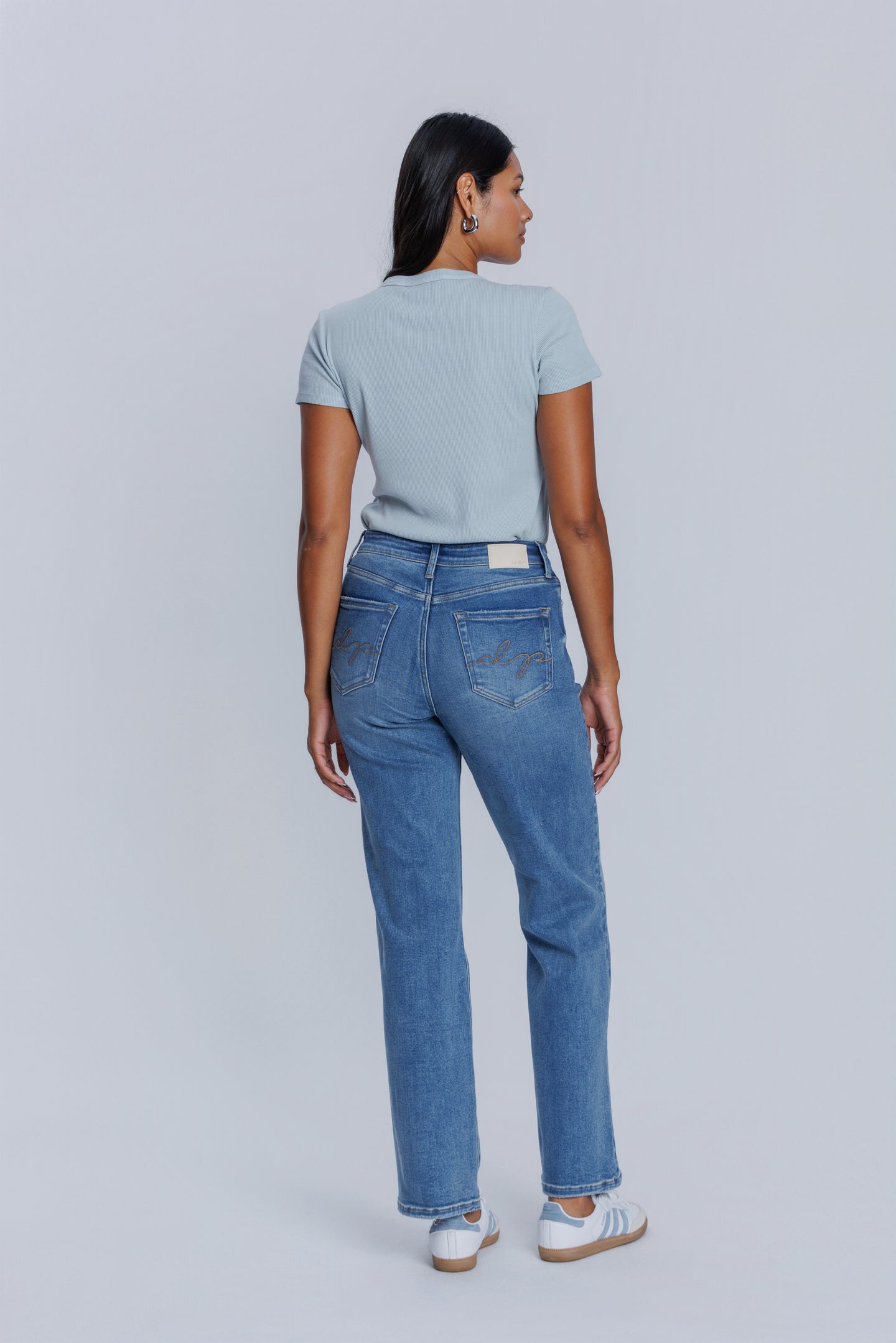 Woman showing her backside wearing a DePart light blue tee and blue jeans against a plain background