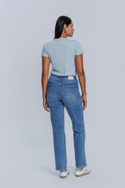 Woman showing her backside wearing a DePart light blue tee and blue jeans against a plain background