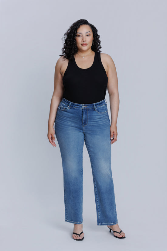Woman wearing a DePart black tank top and blue jeans against a plain background | model-size: 16