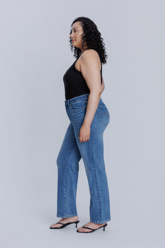 Woman standing sideways wearing a DePart black tank top and blue jeans against a plain background