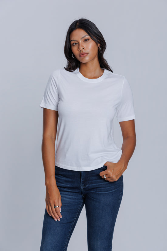 Woman wearing a DePart white t-shirt and dark blue jeans against a light gray background | model-size: 4