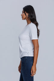 Woman wearing a DePart white t-shirt and dark blue jeans against a light gray background